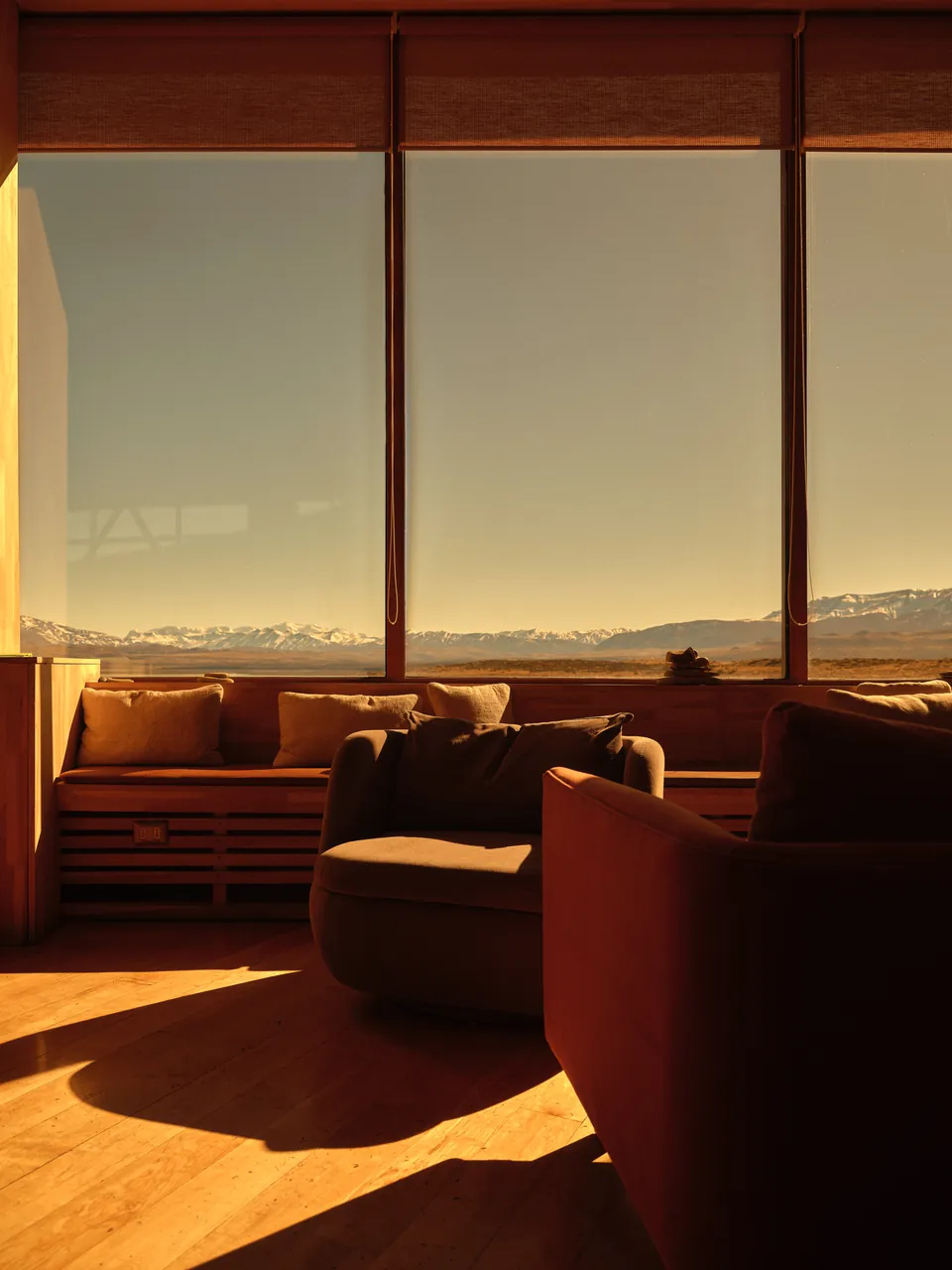Lounge with low sofas facing a wall of glass, mountains at sunset