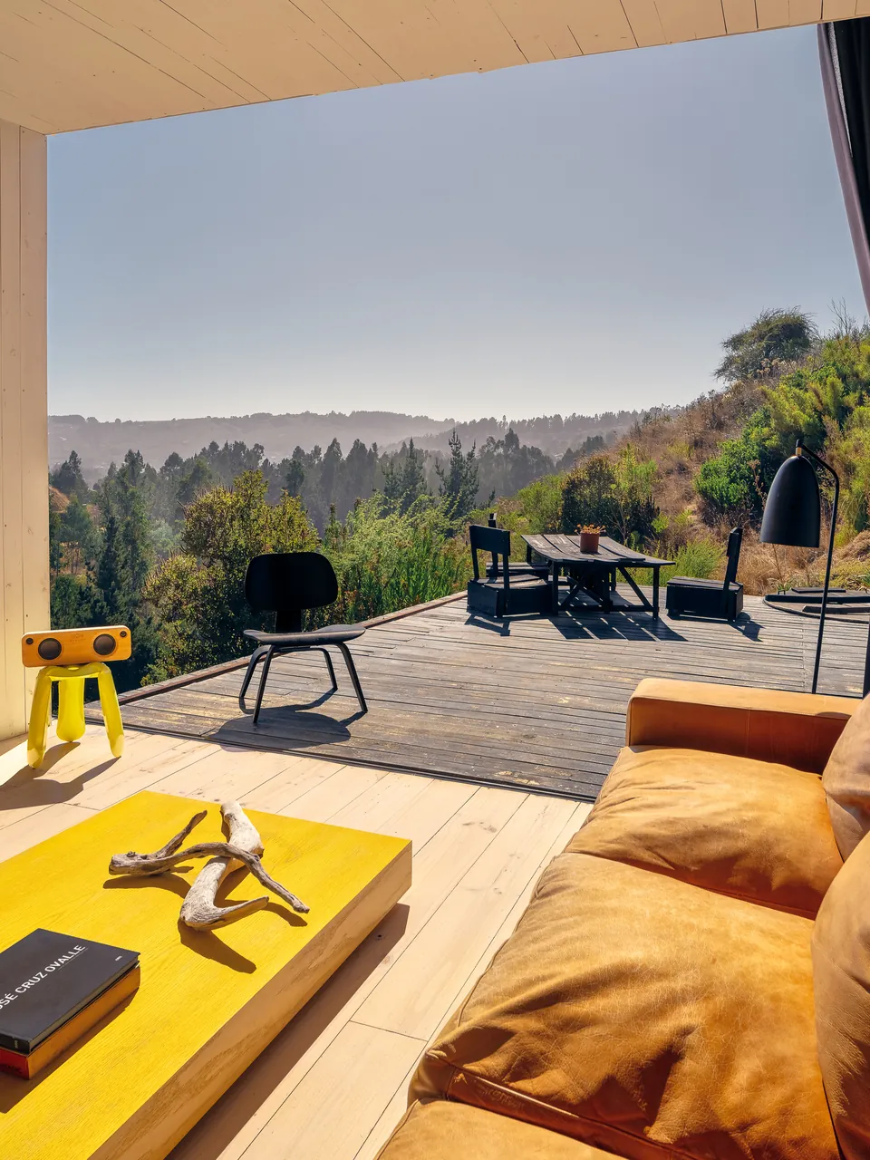 Living room opening to a deck, yellow coffee table, hills beyond