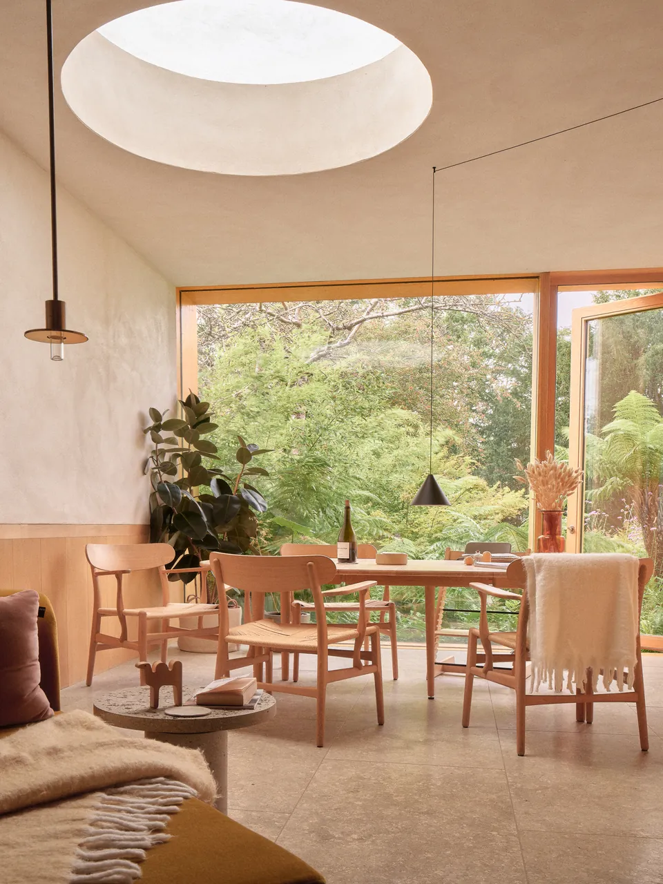 Dining room under a round skylight, garden through timber-framed glass
