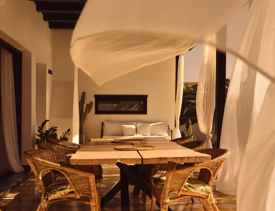 Linen canopy lifting in the breeze above a wicker dining table