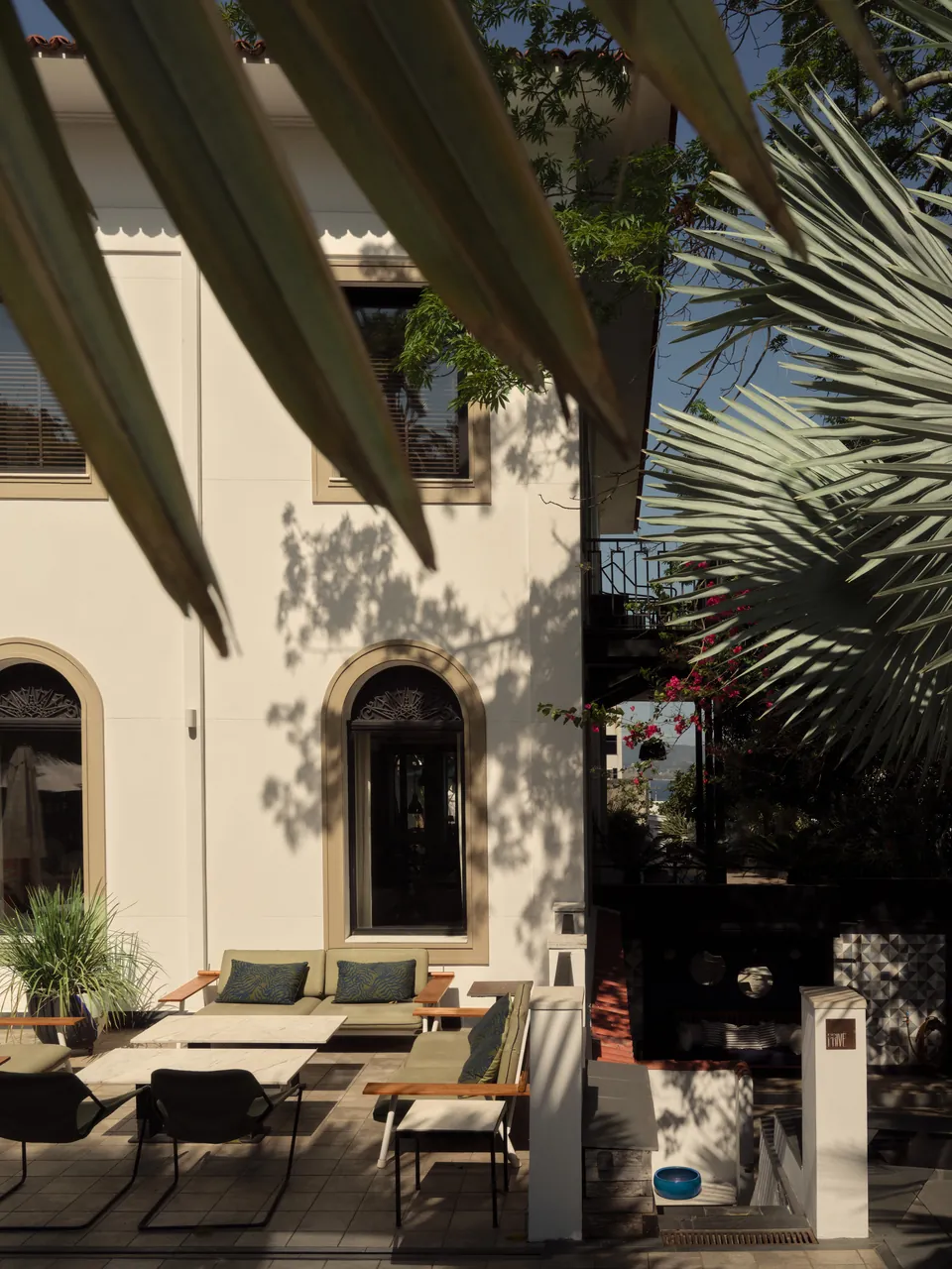 White villa facade through palm fronds, terrace set for lunch