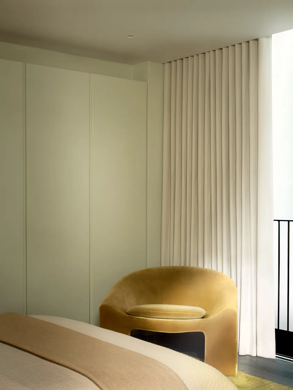 Bedroom corner with an ochre armchair beside sheer curtains