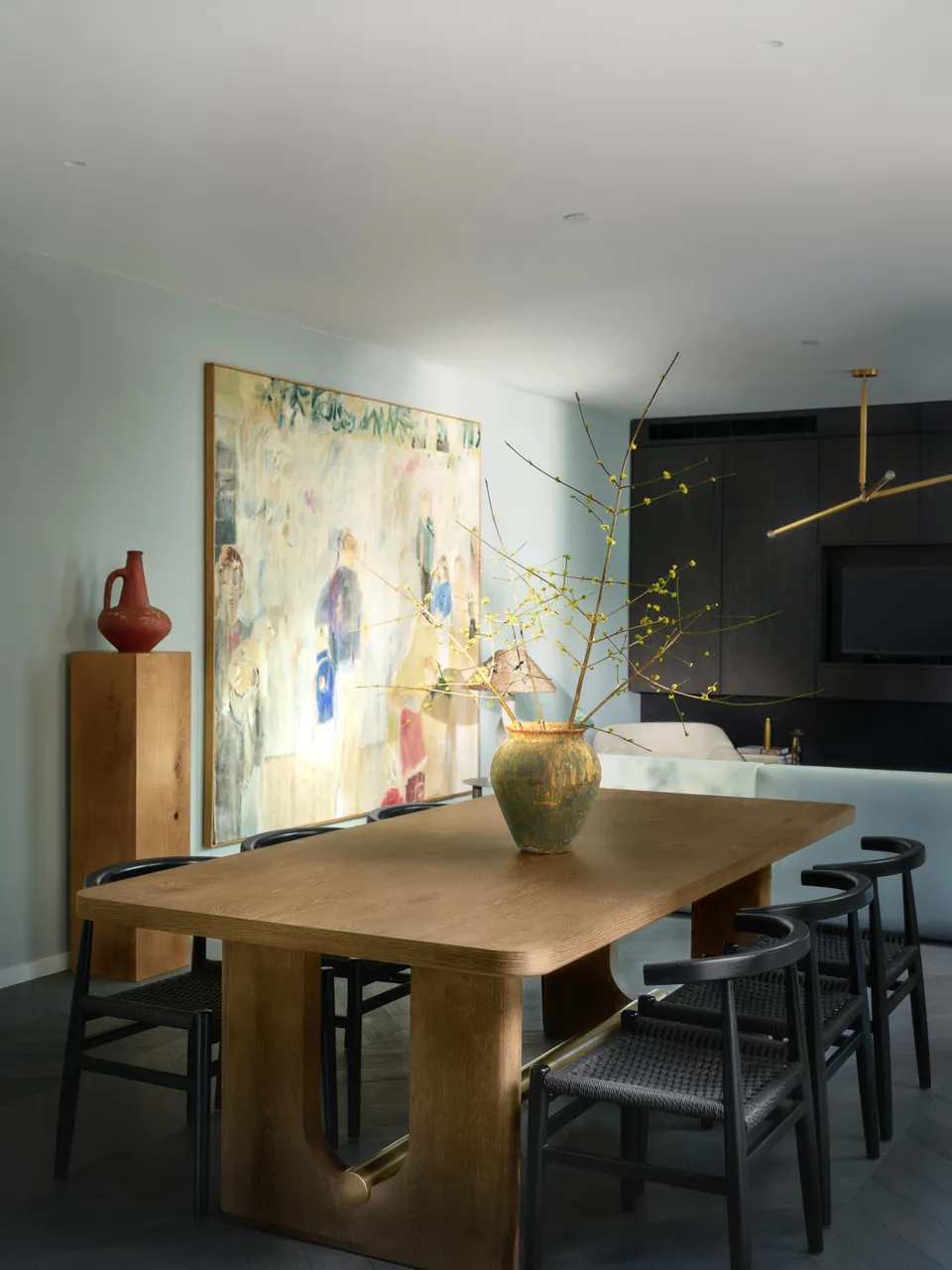 Dining table beneath a large painting, a ceramic vase of branches