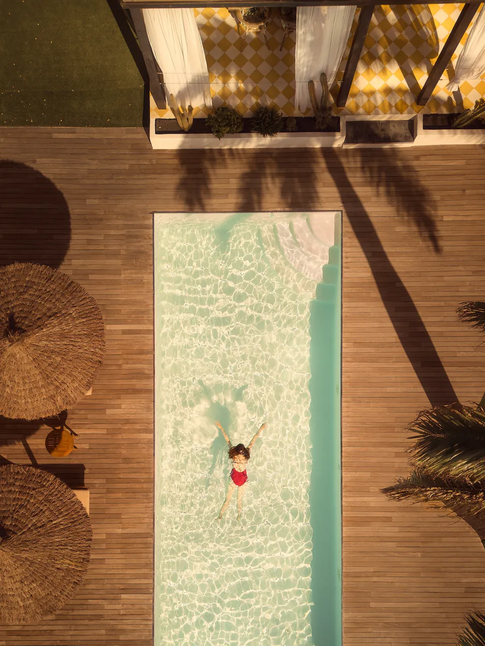 Swimmer from above in a narrow pool between parasols