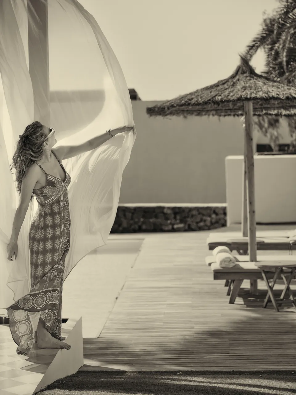 Woman holding a billowing curtain on a pool terrace, black and white