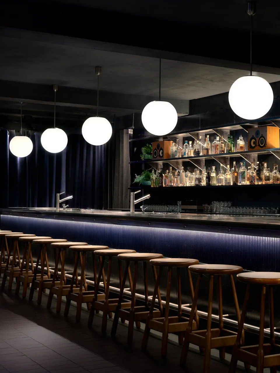 Backlit bar shelves and stools under globe pendants