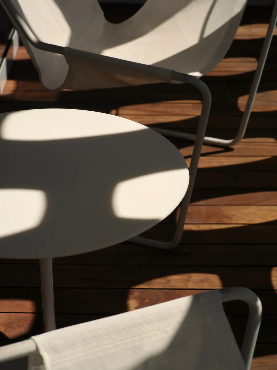 White chairs and a table in hard shadow on a timber deck