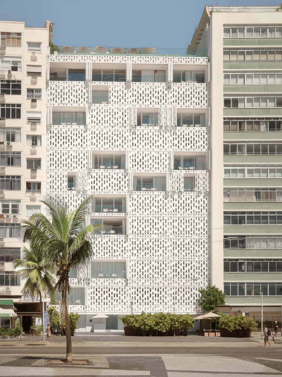 A white perforated façade among the apartment blocks of Copacabana, a palm in front