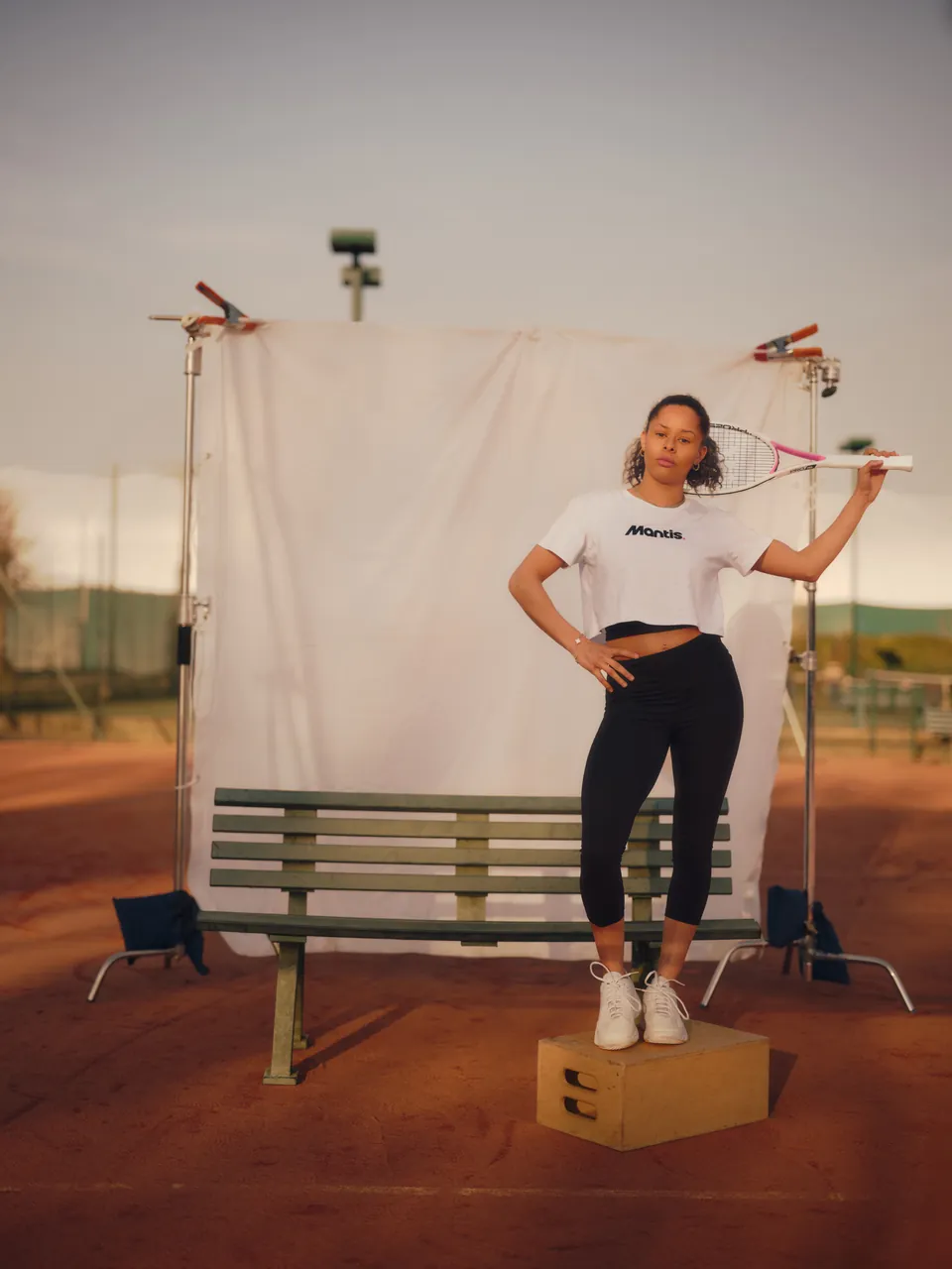 A player in Mantis kit before a white backdrop on a clay court