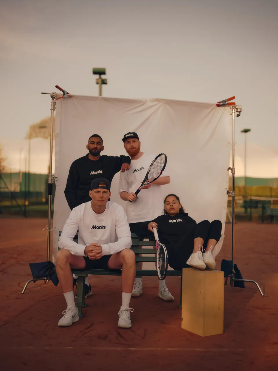 Four players seated before a white backdrop on a clay court