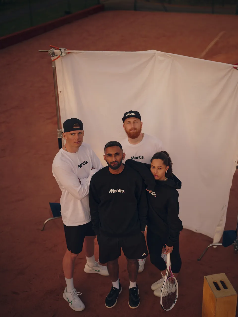 Four players standing before a white backdrop on a clay court