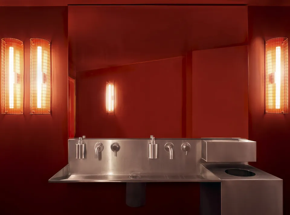 A red washroom with a steel basin and glowing wall lights