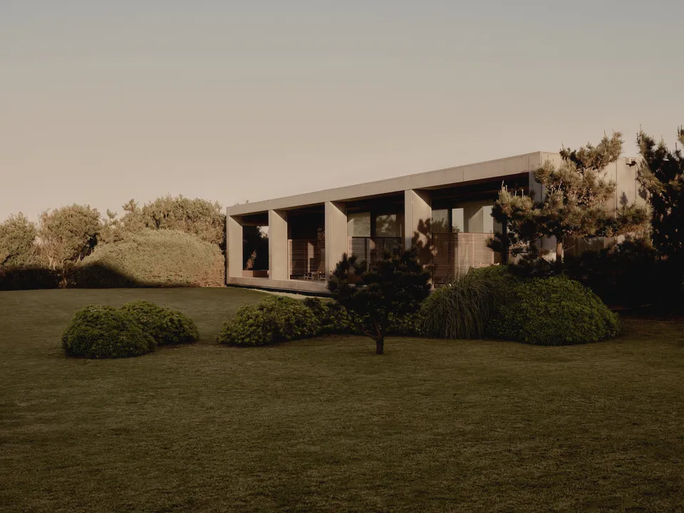A low building beyond a lawn and planting at dusk