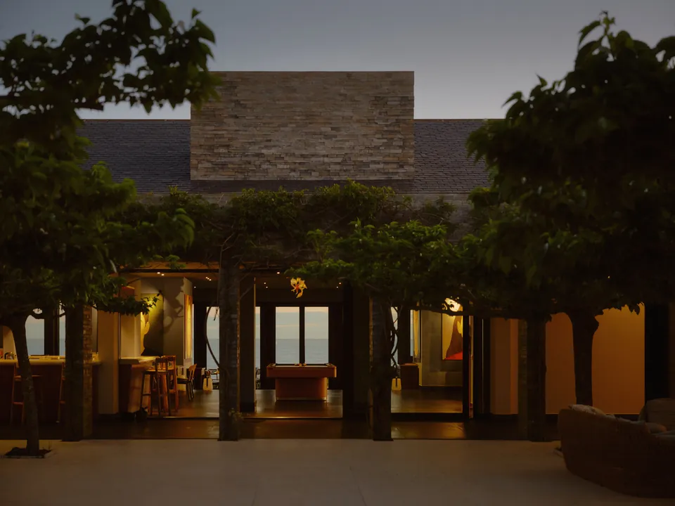 A stone-topped house among trees at dusk, its rooms lit